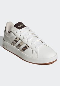 Bijela sportska cipela s glatkim kožnim gornjim dijelom, ukrašena smeđim prugama s leopardskim uzorkom, bijelim vezicama i smeđim logotipom na jeziku.