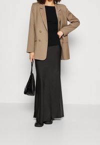 Blazer beige à double boutonnage, top noir côtelé, jupe en satin noire fluide et sac à main noir, assortis à des chaussures plates noires.