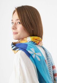 Écharpe colorée avec des motifs floraux et rayés en bleu, jaune et rouge. Tissu léger et transparent qui se drape de manière décontractée autour du cou.