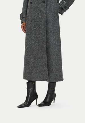 Długi szary wełniany płaszcz z podwójnymi guzikami, noszony z czarnymi skórzanymi botkami z ostrym noskiem, średnim obcasem i bocznymi zamkami.