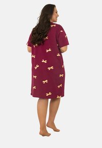 Sukienka nocna z krótkim rękawem, do kolan, w bordowym materiale z żółtymi wzorami w kokardy, o luźnym kroju i miękkiej teksturze.