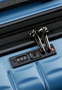 Valise rigide de couleur bleu clair, avec une surface texturée, deux zips noirs, et un système de verrouillage approuvé par la TSA pour la sécurité.