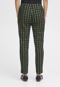 Pantalons noirs fuselés avec un motif pied-de-poule vert, taille haute, poches arrière et texture lisse. Associés à des chaussures noires.