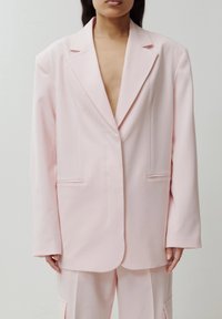 Lichtroze blazer met afgeknipte revers, enkele knoopsluiting en twee voorzakken. Heeft een losse pasvorm en een gladde textuur.