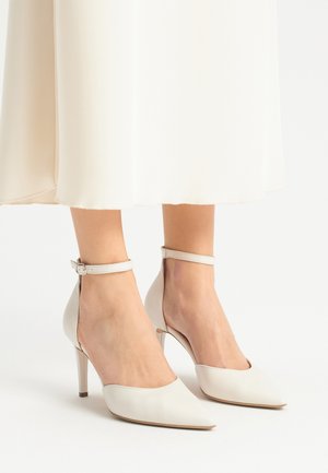Białe skórzane buty na wysokim obcasie z ostrym czubkiem i paskiem wokół kostki, o gładkiej fakturze i smukłym obcasie typu stiletto.