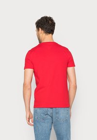 Rød bomulds t-shirt med korte ærmer, en rund hals og et enkelt design. Båret sammen med blå denim jeans, der viser en glat tekstur.