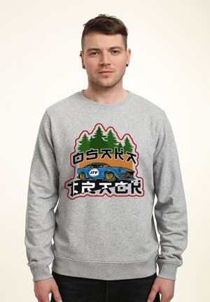 Sweatshirt gris avec un design graphique d'une voiture bleue et d'arbres verts, texte en gras, col rond et poignets côtelés.
