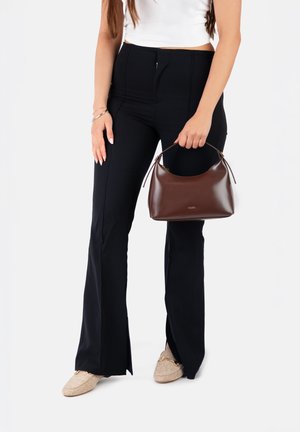 Vrouw draagt zwarte wijde broek, witte mouwloze top, beige loafers en houdt een bruine leren handtas vast aan het hengsel.