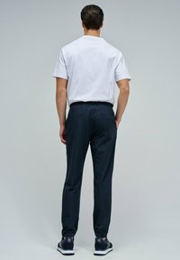 Conjunto masculino que incluye una camiseta blanca de cuello redondo y pantalones con cintura elástica en color marino, con bolsillos traseros, complementados con zapatillas oscuras.
