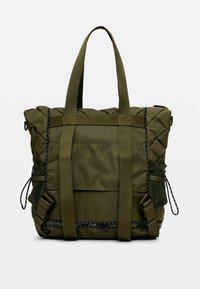 Sac fourre-tout matelassé vert olive avec deux poignées supérieures, poche en maille externe, sangles renforcées et accents en matériel noir.