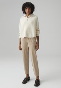 Cream ribbed knit pullover with a half-zip collar, paired with beige trousers featuring side pockets and brown loafers.
