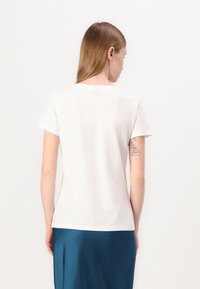 Tricou alb cu mânecă scurtă și guler rotund. Material din bumbac neted. Vederea din spate arată un design simplu, fără modele sau accente.