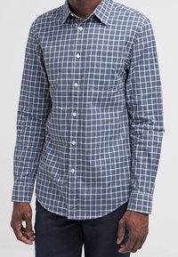 Långärmad knapp-up skjorta i marinblå och grön rutigt mönster, med spetsig krage, bröstficka och vita knappar. Bekväm tyg.