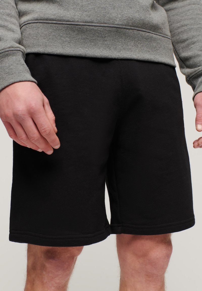 Shorts neri in cotone con una vita elastica, caratterizzati da una superficie liscia e un design fino al ginocchio. I bordi cuciti sono visibili.