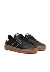Mustan nahast sneakers, millel on tekstureeritud pind, valge kontsakaunistus, kummi rubberist tald ja lipsukujundus. Omab logo keelel ja külgpaneelil.
