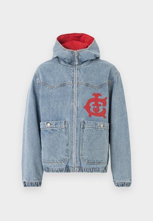 Lys blå denimjakke med glidelås foran, to lommer med knapper, elastiske mansjetter og midje, rød indre hettefôr og rød grafikk på venstre bryst.