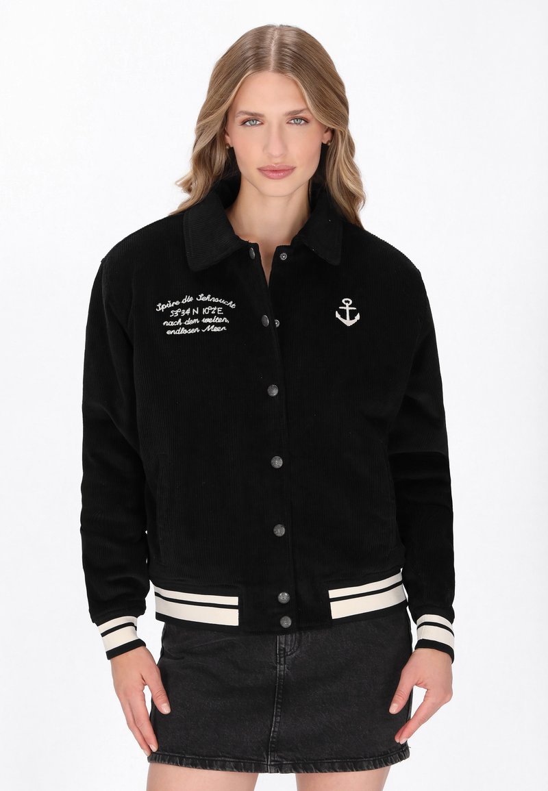 Czarna kurtka z korduroju z kołnierzem, z przodu na guziki, białym haftem kotwicy i paskowymi mankietami. Tekst na klatce piersiowej dodaje szczegółu.