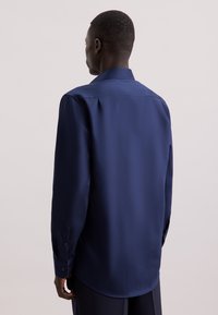 Camicia da uomo in satin blu navy con colletto aperto, maniche lunghe e polsini con bottone. Tessuto liscio con vestibilità su misura e orlo curvo.