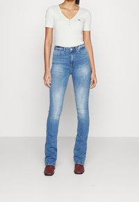 Světle modré džínové kalhoty s mírným vyblednutím a prošoupáním, spárované s bílým krátkým rukávem s ribovaným vzorem a výstřihem do V, doplněné o knoflíkový detail.