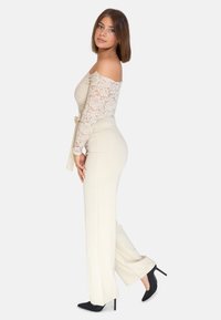 Body in pizzo off-the-shoulder color crema abbinato a pantaloni a gamba larga color crema e tacchi a stiletto neri. Texture morbide e silhouette aderente.