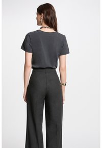 T-shirt en coton gris avec une coupe décontractée et des manches courtes, associé à un pantalon large taille haute gris foncé avec une poche arrière.