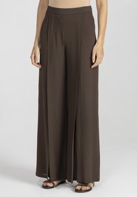 Brązowe spodnie o szerokich nogawkach, wykonane z gładkiego, lekkiego materiału, z wysokim stanem oraz pionowymi plisami, z bocznymi rozcięciami dla ułatwienia ruchu.