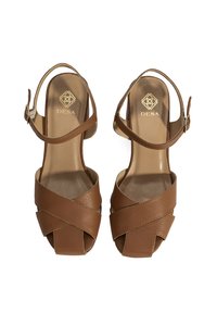 Braune Leder-Absatzsandalen mit gekreuztem Riemendesign, offener Zehenpartie und Knöchelriemen. Goldenes Logodetail auf der Innensohle. Glatte Textur.