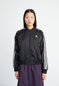 Black satin bomber jacket with white stripe accents on sleeves and a zip closure. Features a ribbed collar and logo on the chest.