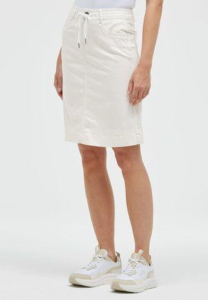 White knee-length skirt with front pockets and drawstring waist, worn with white and beige sneakers on a standing person.