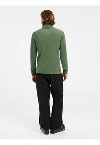Maglione verde in pile a maniche lunghe con colletto alto, abbinato a pantaloni neri. Tessuto testurizzato, design aderente e minimale branding sull'orlo.