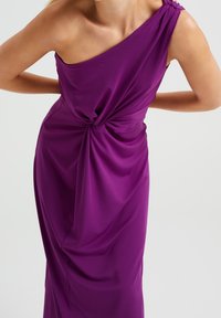 Fioletowa sukienka na jedno ramię z drapowanym materiałem i węzłem w talii. Gładka tekstura, dopasowany krój i minimalne akcenty metalowe.