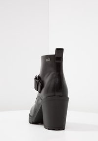 Botas de tobillo de cuero negro con un alto tacón cuadrado, que cuentan con un detalle de hebilla lateral y una asa en la parte posterior para ponérselas fácilmente.