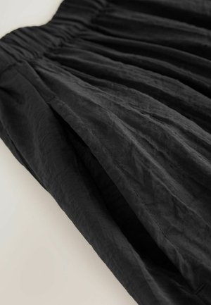 Falda negra con tejido texturizado y arrugado, cintura fruncida y pliegues fluidos que ofrecen una silueta relajada.