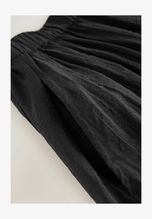 Czarna spódnica z teksturowanej, pomarszczonej tkaniny, z marszczonym pasem i swobodnymi plisami, tworzącymi luźny sylwetkę.