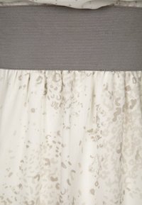 Lehký krémový šaty s texturovaným šedým elastickým pasem, na kterých se nachází rozptýlený šedý skvrnitý vzor.