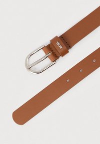 Καφέ δερμάτινη ζώνη με ασημί μεταλλική αγκράφα, διακοσμημένη με μία μεταλλική θηλιά και πολλαπλές τρύπες για ρύθμιση μεγέθους, με χαραγμένη την ένδειξη «BOSS».