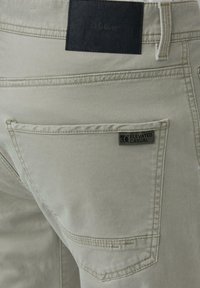 Lichtgrijze broek heeft twee achterzakken met een zwart leren label. Het materiaal lijkt zacht en glad met subtiele stikseldetails.