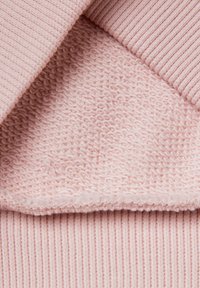 Jasnoróżowy materiał o dwóch teksturach: na wierzchu prążkowany splot, a poniżej miękki, tkany wzór, pokazujący gładkie i teksturowane powierzchnie.