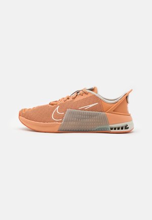 Pomarańczowy, niskoprofilowy but sportowy z cholewką z siateczki, szarym przezroczystym panelem podeszwy środkowej, białym logo Nike i amortyzowanym wsparciem pięty.
