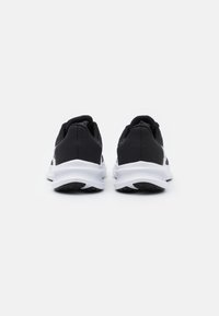 Zapatos deportivos negros con una parte superior de malla, una media suela blanca y una suela exterior de goma texturizada, con un logo sutil en el costado.