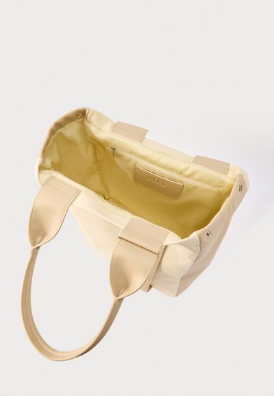 Μπεζ τσάντα χειρός με δύο υφασμάτινες λαβές, ανοιχτό πάνω μέρος που αποκαλύπτει το εσωτερικό με ανοιχτό κίτρινο επένδυση και εσωτερική τσέπη με φερμουάρ.