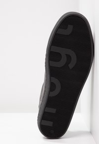 Svart gummisko sula med texturerat grepp, med ett tydligt logomönster och en låg profil design.