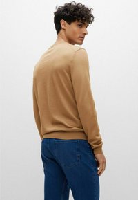 Maglione a maglia marrone con maniche lunghe, scollatura rotonda e orlo a coste, abbinato a jeans in denim blu. Texture liscia e silhouette aderente.