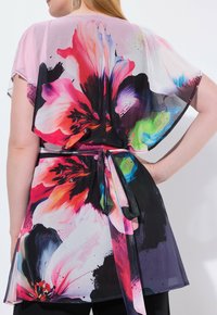 Femme portant un blouse en voile à motifs floraux avec des manches larges et une ceinture nouée à la taille, montrant la vue de dos.