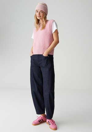 Pink knitted vest over a white shirt, paired with dark denim wide-leg pants and pink sneakers with black stripes.