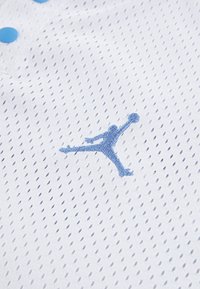 White mesh fabric features blue embroidered Jumpman logo. Small blue buttons are visible, highlighting a sporty design with breathability.