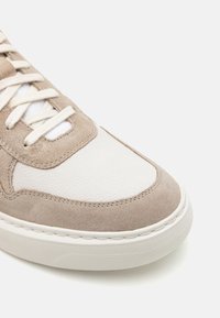 Γκρι σουέτ και λευκά δερμάτινα αθλητικά παπούτσια με στρογγυλή μύτη, επίπεδα κορδόνια και υφή καουτσούκ στη σόλα. Διαθέτει πάνελ από αντίθετα υλικά.