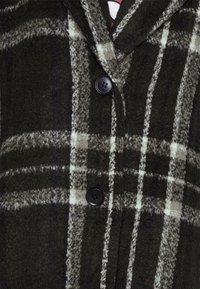 Zwart-wit geruite wollen jas met een gestructureerde stof, notch revers en twee zwarte knopen aan de voorkant.