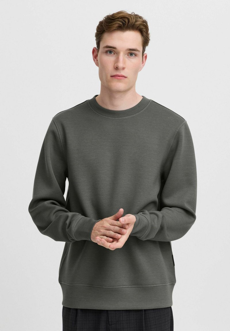 Donkergroene sweatshirt van zachte stof, met een ronde halslijn en lange mouwen. Het ontwerp bevat ribgebreide manchetten en zoom.