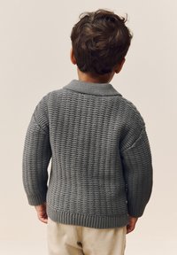 Gray knitted sweater featuring a textured pattern, ribbed cuffs, and neckline, shown from the back on a person with brown hair.